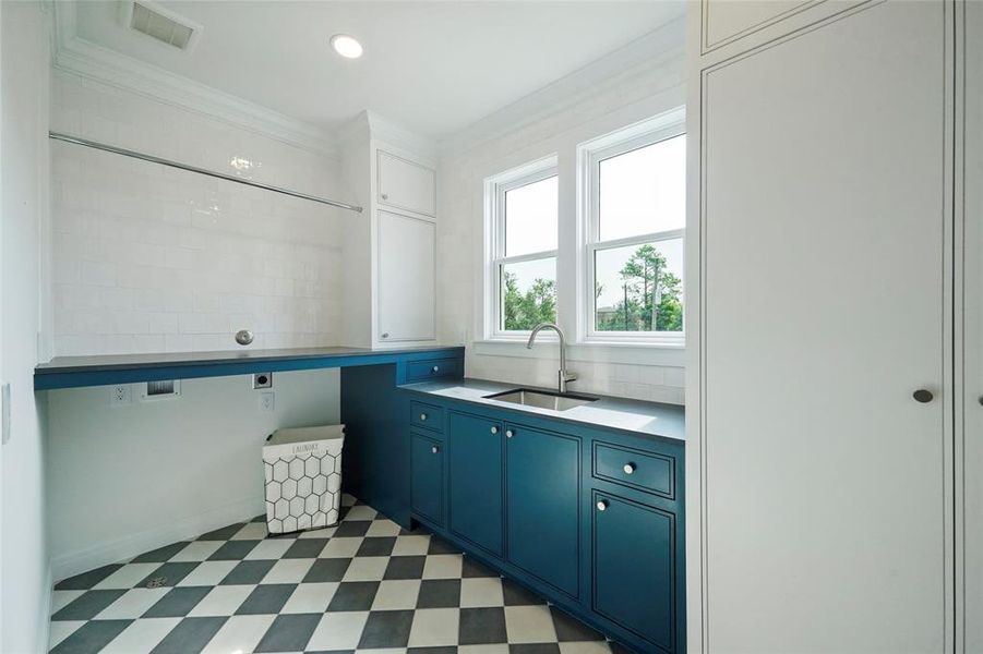 Bright laundry room with playful black and white tile, blue cabinetry, white walls, ample storage, and natural light from windows. Inviting and functional space.