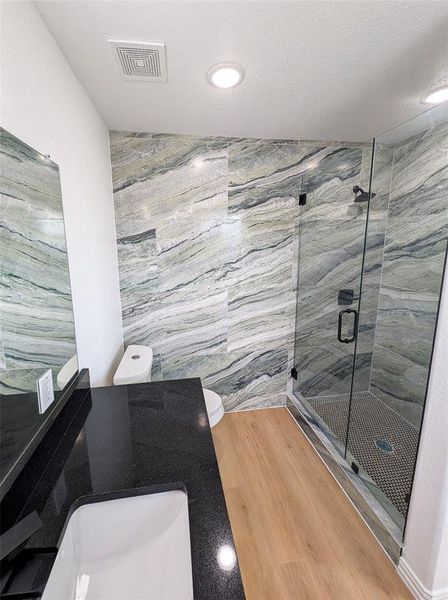 Bathroom featuring toilet, tile walls, wood-type flooring, sink, and a shower with door