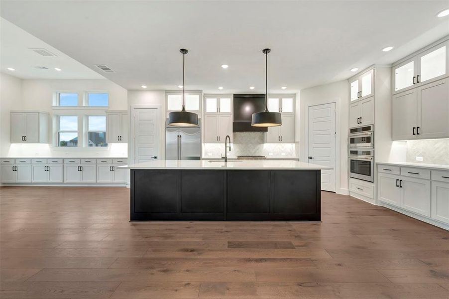 Kitchen featuring glass insert cabinets, decorative backsplash, decorative light fixtures, dark wood-style flooring, and two tone cabinetry