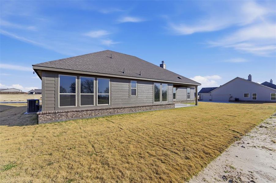 Back of house featuring brick siding, a yard, a patio, and roof with shingles