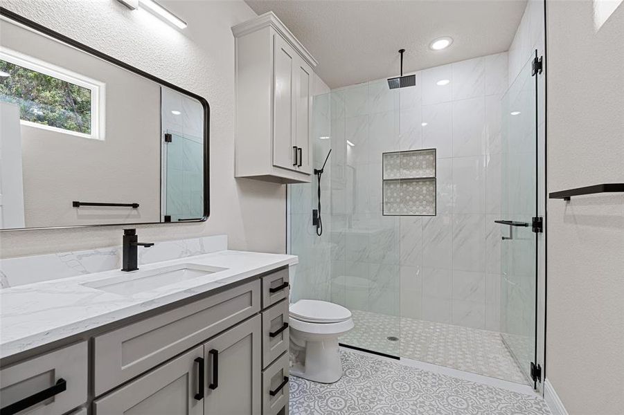 Bathroom featuring tile patterned floors, toilet, a shower with door, and vanity