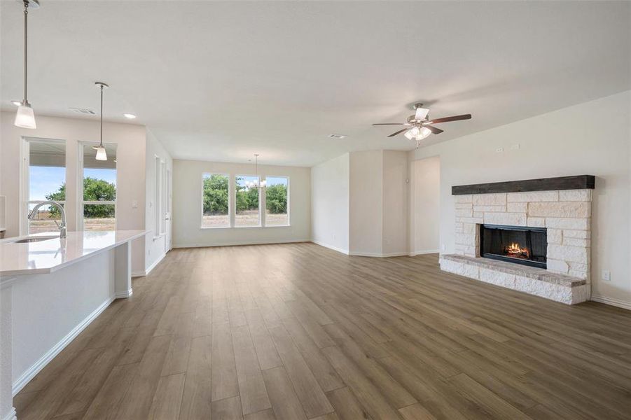 Unfurnished living room with a stone fireplace, light wood-type flooring, a chandelier, recessed lighting, and ceiling fan