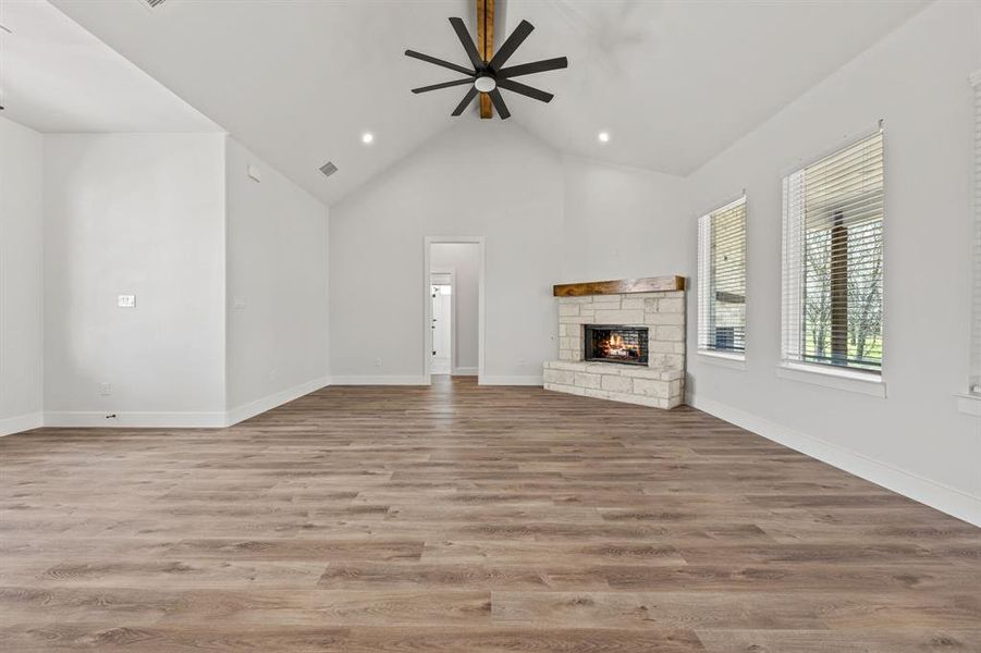 Unfurnished living room featuring a stone fireplace, wood finished floors, ceiling fan, high vaulted ceiling, and recessed lighting Unfurnished living room featuring a stone fireplace, wood finished floors, ceiling fan, high vaulted ceiling, and recessed lighting