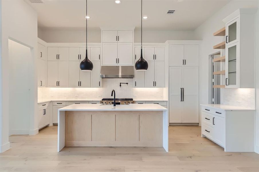 Kitchen with light hardwood / wood-style floors, white cabinetry, tasteful backsplash, decorative light fixtures, and a center island with sink