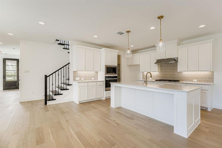 Kitchen featuring range hood, stainless steel appliances, decorative backsplash, light wood-style flooring, and recessed lighting