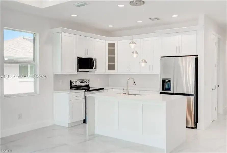 Kitchen featuring white shaker-style cabinetry, a central island with a waterfall edge, stone countertops, stainless steel appliances, and pendant lighting