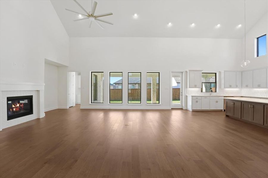 Unfurnished living room with high vaulted ceiling, plenty of natural light, a tiled fireplace, recessed lighting, and dark wood-style floors