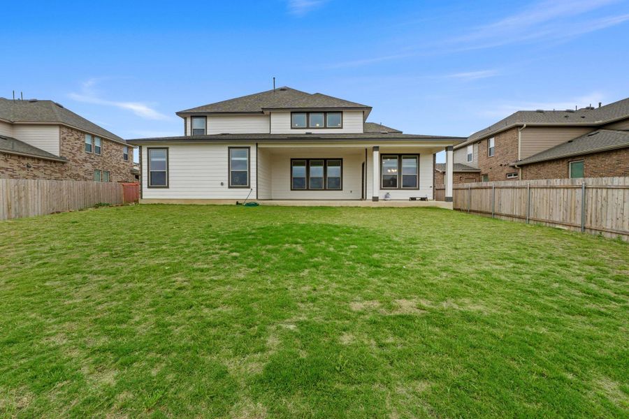 Expansive grassy yard featuring a covered patio, white siding, dark trim windows, and a privacy fence