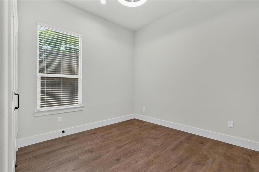 This bright room features wood-finish flooring, a white window frame with blinds, a sleek ceiling light fixture, and light-toned walls with white baseboards