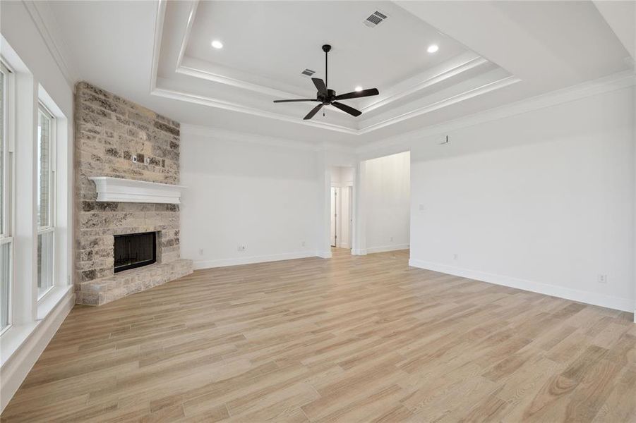 Unfurnished living room featuring ceiling fan, a brick fireplace, a raised ceiling, and ornamental molding