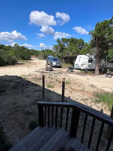 A wooden deck overlooks a natural, undeveloped landscape with sparse trees under a clear sky.