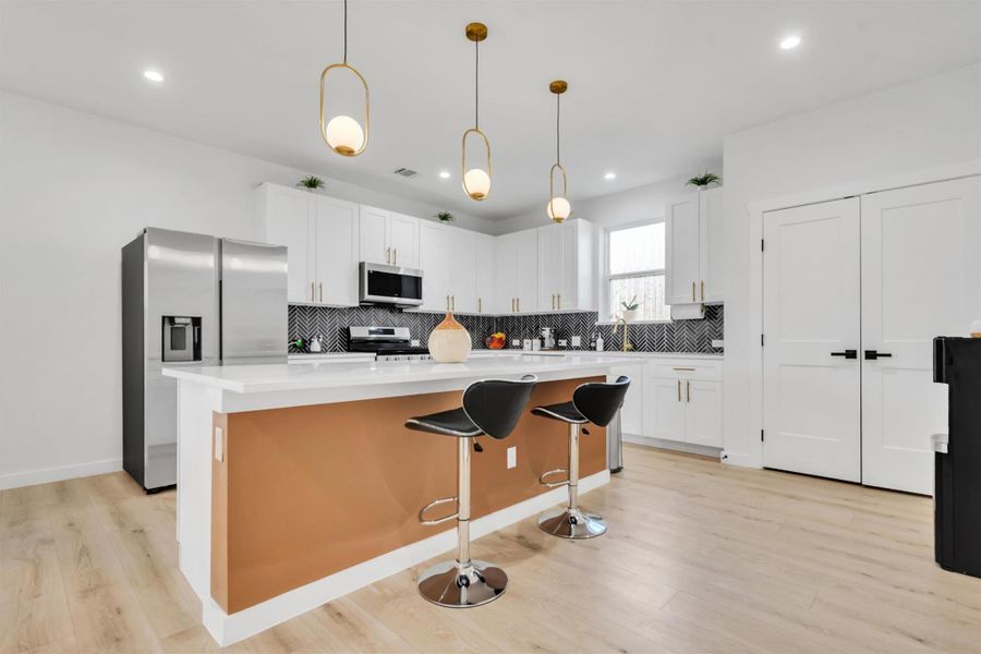 Kitchen with white cabinetry, stainless steel appliances, decorative light fixtures, and a breakfast bar area