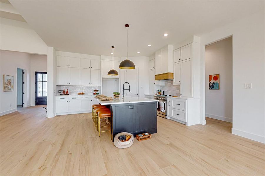 Kitchen with light hardwood / wood-style flooring, a kitchen island with sink, white cabinets, backsplash, and custom exhaust hood