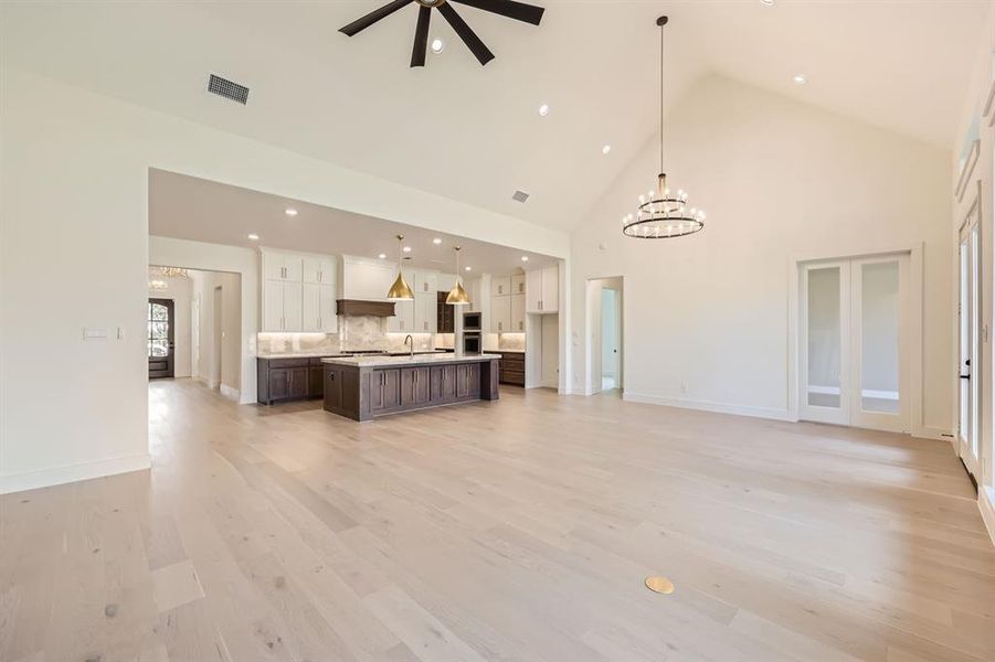 Unfurnished living room with light hardwood / wood-style flooring, high vaulted ceiling, sink, and ceiling fan with notable chandelier