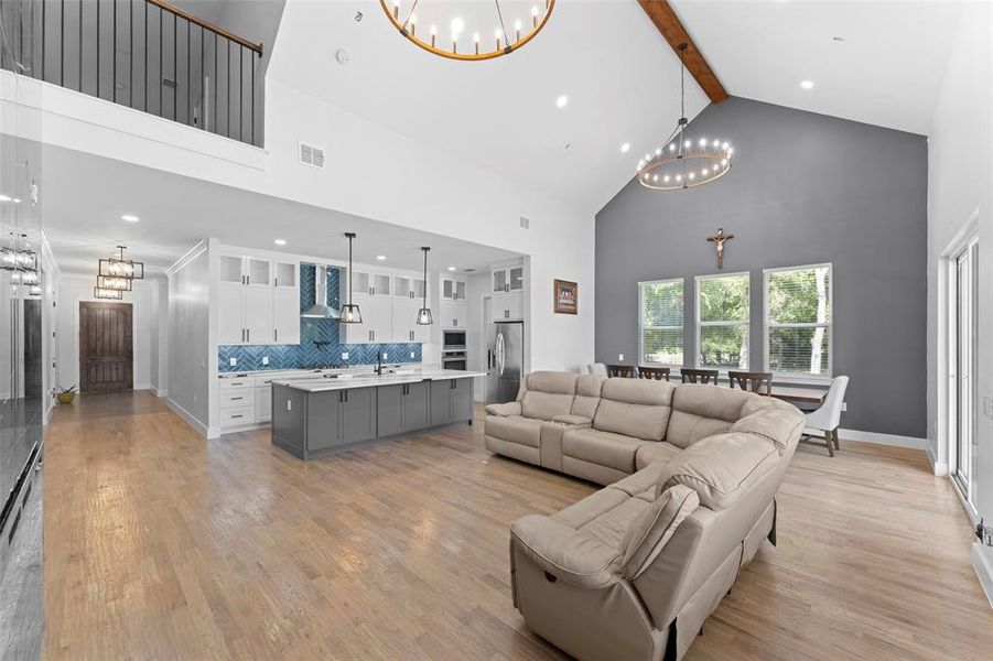 Living room with a chandelier, high vaulted ceiling, beamed ceiling, light wood finished floors, and recessed lighting Living room with a chandelier, high vaulted ceiling, beamed ceiling, light wood finished floors, and recessed lighting
