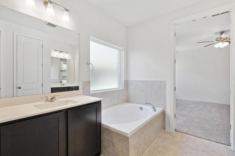 Bathroom with vanity, ceiling fan, tile patterned floors, and a relaxing tiled tub