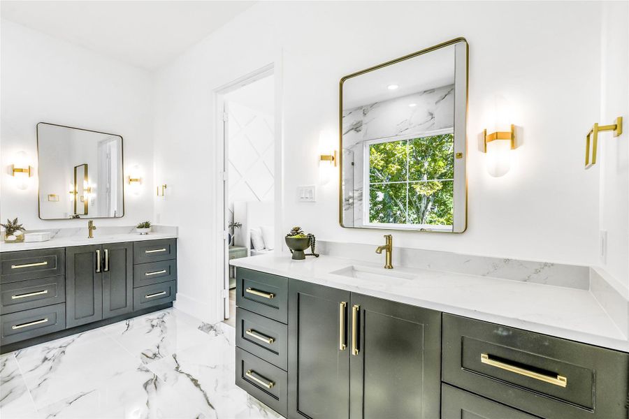 This photo highlights the dual vanities, each with solid quartz countertops, under mount sinks, and brushed brass fixtures. The wall-mounted sconces and oversized mirrors with brass frames reflect natural light beautifully, creating a bright and balanced environment. Every element—down to the precise cabinet craftsmanship and hardware alignment—shows off the meticulous builder attention to finish detail and symmetry.