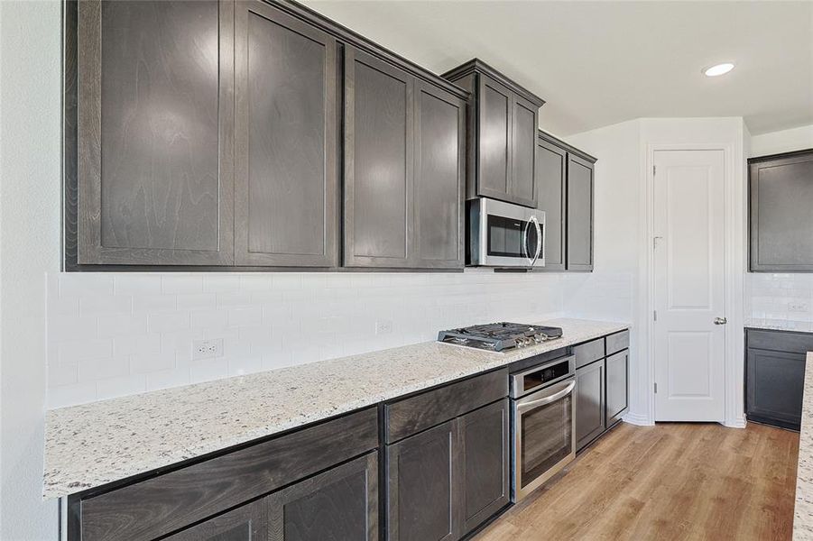 Kitchen featuring light stone counters, stainless steel appliances, light hardwood / wood-style floors, dark brown cabinets, and tasteful backsplash