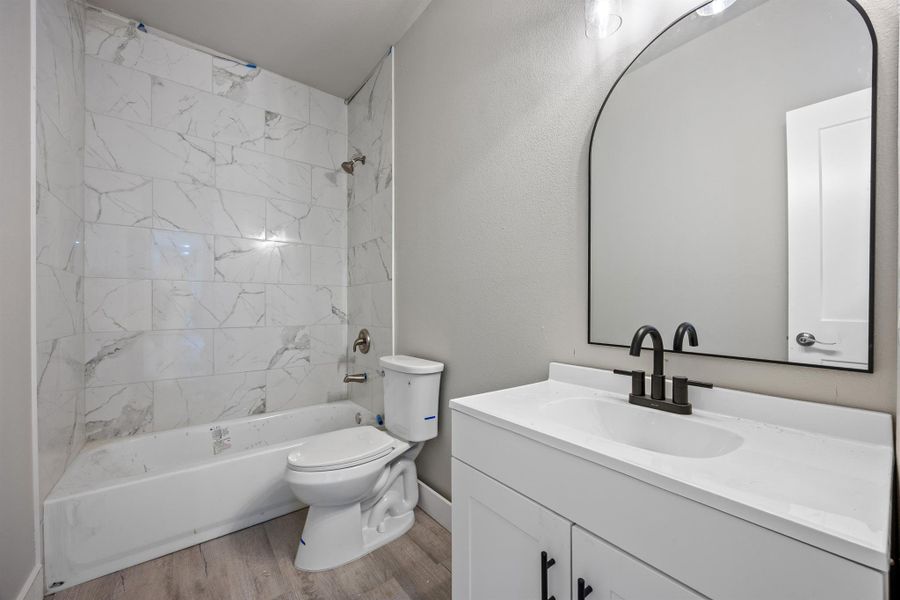 Full bathroom featuring vanity, toilet, wood finished floors, shower / bathing tub combination, and baseboards Full bathroom featuring vanity, toilet, wood finished floors, shower / bathing tub combination, and baseboards