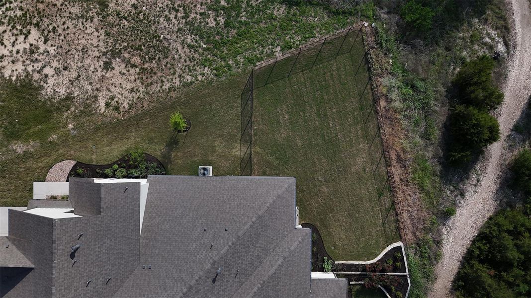 Aerial view showcasing the property's roof with dark grey shingles, a manicured lawn, and a fenced yard