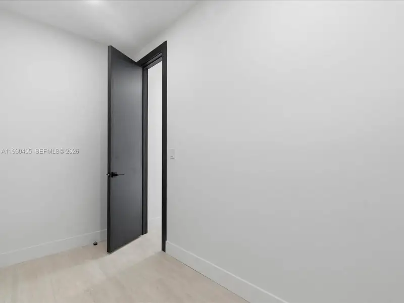 Neutral-toned walls, light-finished flooring, and a solid-core interior door featuring a matte black lever handle and matching door casing Neutral-toned walls, light-finished flooring, and a solid-core interior door featuring a matte black lever handle and matching door casing