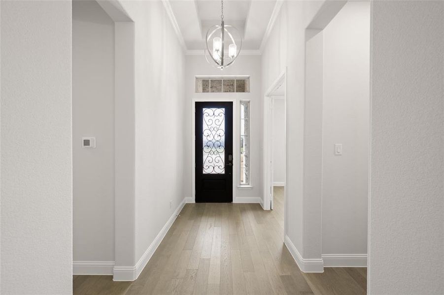 Foyer entrance featuring wood finished floors, a chandelier, baseboards, and ornamental molding Foyer entrance featuring wood finished floors, a chandelier, baseboards, and ornamental molding