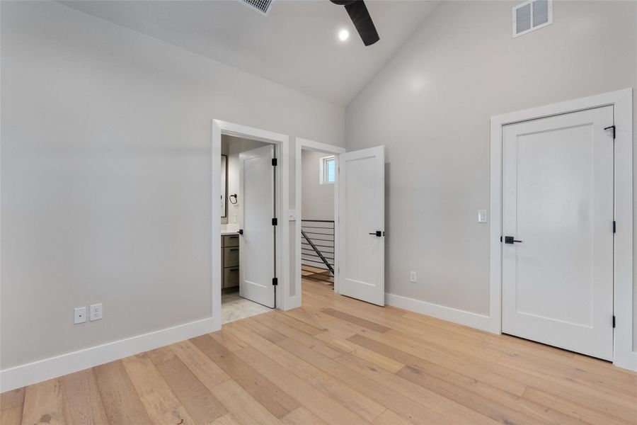 Spacious primary bedroom featuring vaulted ceilings, light wood-finish flooring, white baseboards, and white interior doors with matte black hardware. A full private en-suite bathroom and walk-in closet. Spacious primary bedroom featuring vaulted ceilings, light wood-finish flooring, white baseboards, and white interior doors with matte black hardware. A full private en-suite bathroom and walk-in closet.