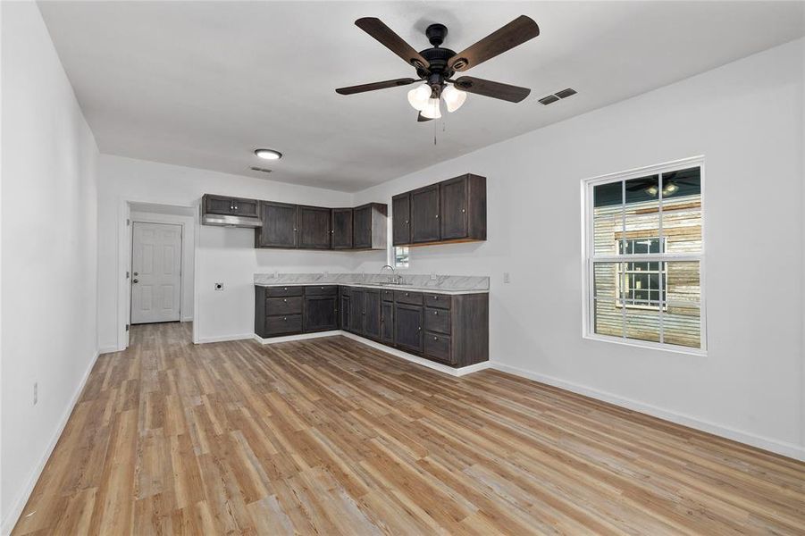 Kitchen featuring dark brown cabinets, light wood-type flooring, light countertops, and a ceiling fan Kitchen featuring dark brown cabinets, light wood-type flooring, light countertops, and a ceiling fan