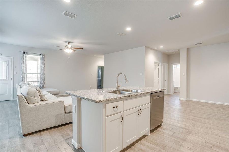 Kitchen featuring open floor plan, white cabinets, recessed lighting, a center island with sink, and light stone countertops