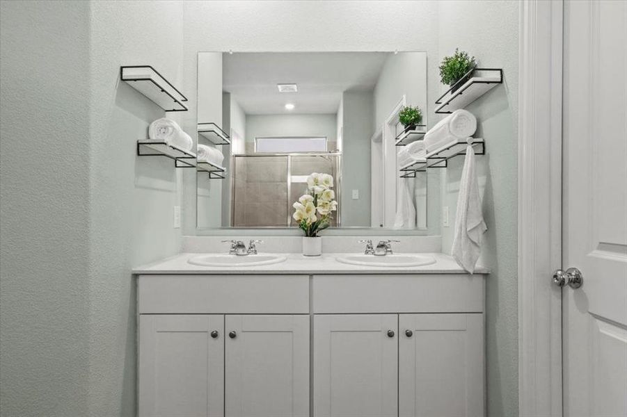 Full bath with double vanity, tiled shower, and a textured wall