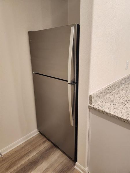 Kitchen with freestanding refrigerator, light wood-style flooring, and light stone counters Kitchen with freestanding refrigerator, light wood-style flooring, and light stone counters