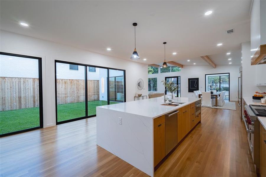 Kitchen featuring a large island with sink, light wood-type flooring, hanging light fixtures, and appliances with stainless steel finishes