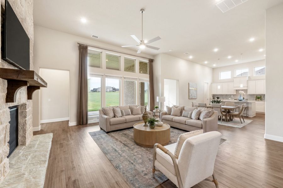 Open-concept living room with stone fireplace, high ceilings, and hardwood floors, open to dining area and kitchen