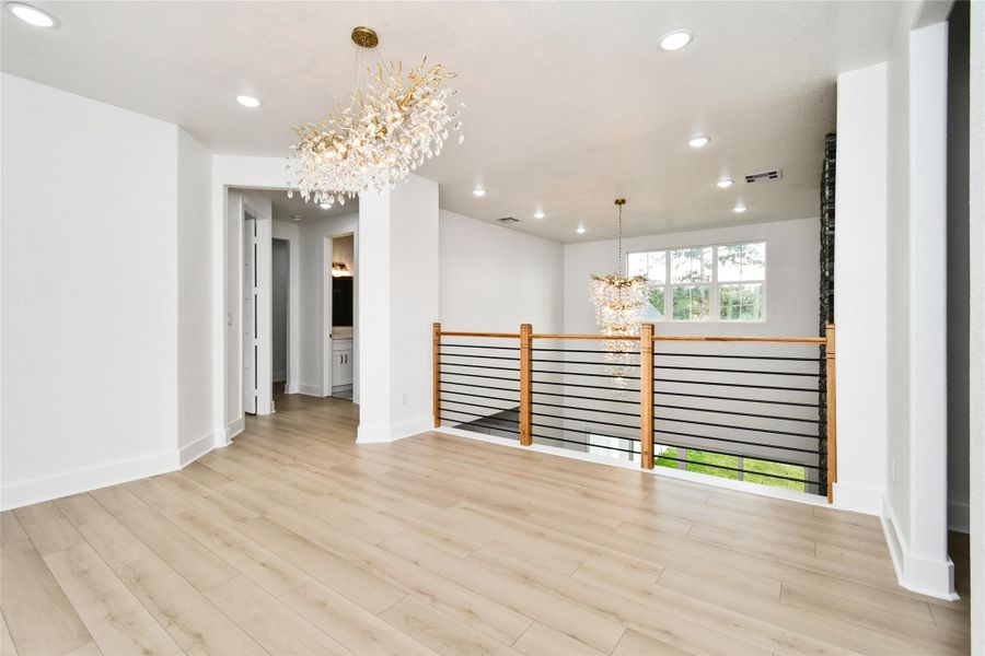An architectural landing overlooks the main living area, featuring a modern horizontal cable railing system with warm wood accents. The open-air design maintains a seamless connection between levels while highlighting the home's impressive lighting collection.