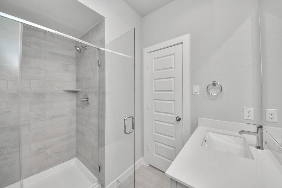 Secondary bath features tile flooring, walk-in shower with tile surround, light stained wood cabinets, beautiful light countertop. Sample photo of completed home with similar floor plan. Actual colors and selections may vary.