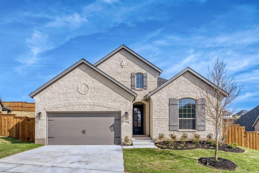 French country style house featuring an attached garage, concrete driveway, and brick siding