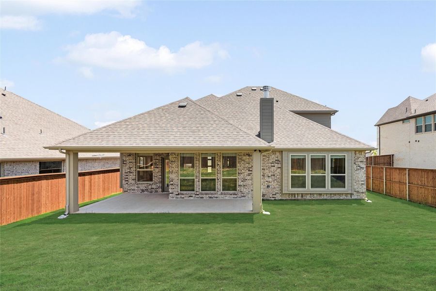 Rear exterior of brick home with covered patio, green lawn, and wood privacy fence Rear exterior of brick home with covered patio, green lawn, and wood privacy fence