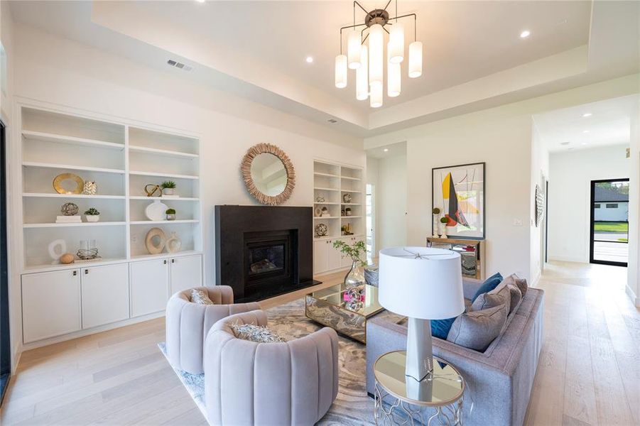 Living room featuring an inviting chandelier, built in shelves, a tray ceiling, and light wood-type flooring