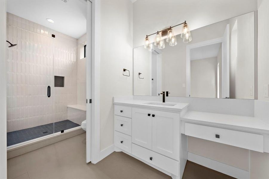 En-suite bath has a shower with bench and walls clad in dimensional tile. Quartz counters with a seated vanity.