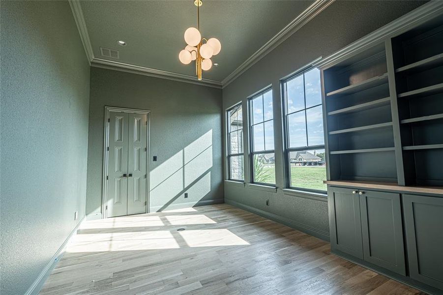 Unfurnished room with ornamental molding, a textured wall, a chandelier, and light wood-type flooring Unfurnished room with ornamental molding, a textured wall, a chandelier, and light wood-type flooring