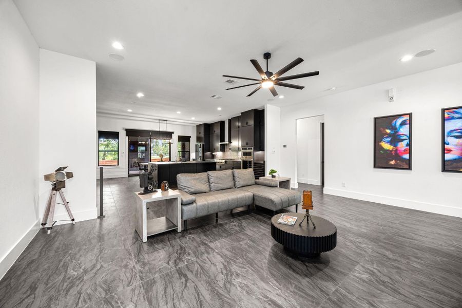 Spacious, modern living area with sleek dark flooring and an open layout. The kitchen in the background is equipped with custom cabinetry and stainless-steel appliances. Large windows provide ample natural light. Spacious, modern living area with sleek dark flooring and an open layout. The kitchen in the background is equipped with custom cabinetry and stainless-steel appliances. Large windows provide ample natural light.