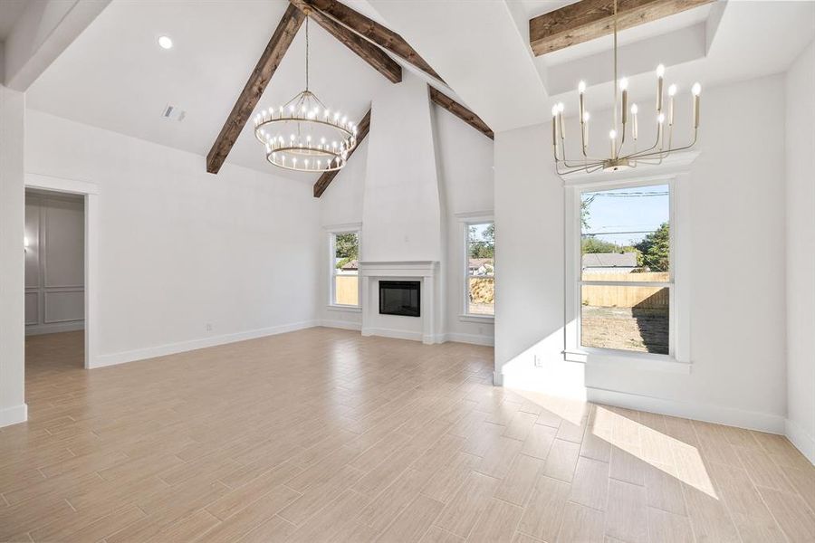 Unfurnished living room with a chandelier, high vaulted ceiling, beam ceiling, wood tiled floors, and a large fireplace
