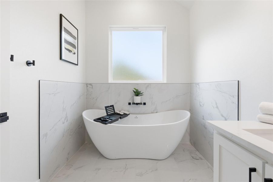 Full bath with vanity, light marble finish floors, a freestanding tub, and tile walls