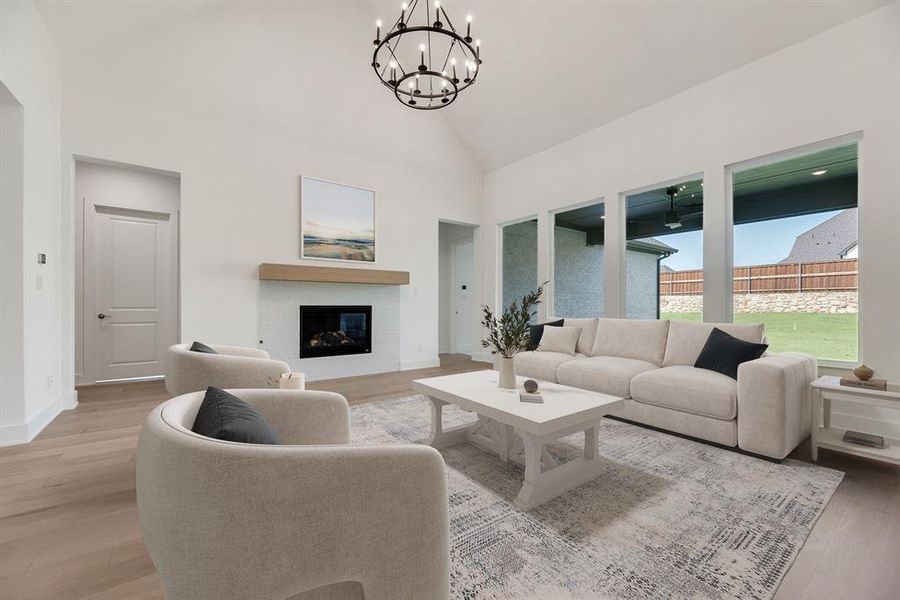 Living area featuring light wood-type flooring, high vaulted ceiling, a glass covered fireplace, and a chandelier