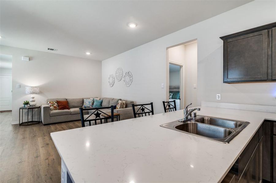 Kitchen featuring wood finished floors, visible vents, a sink, dark brown cabinets, and light stone countertops