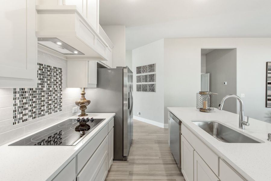 Galley kitchen with white cabinets, mosaic tile backsplash, electric cooktop, and stainless steel sink and refrigerator