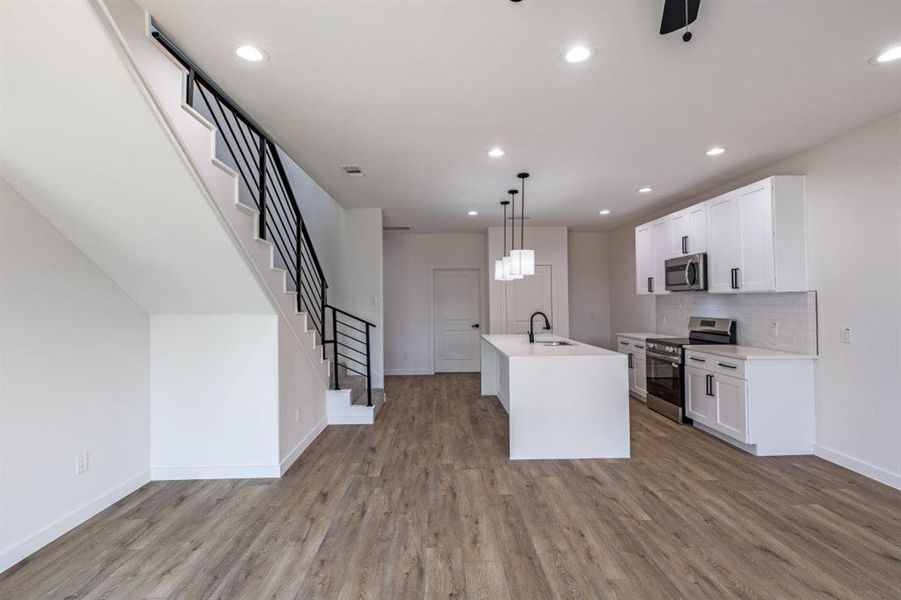 Kitchen featuring stainless steel appliances, white cabinetry, decorative light fixtures, a kitchen island with sink, and tasteful backsplash Kitchen featuring stainless steel appliances, white cabinetry, decorative light fixtures, a kitchen island with sink, and tasteful backsplash