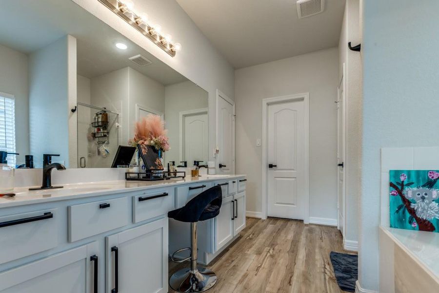 This bathroom features a modern, spacious design with dual sinks, sleek black fixtures, ample cabinet storage, and a large mirror. It includes a glass-enclosed shower and wood-style flooring, creating a stylish and functional space.
