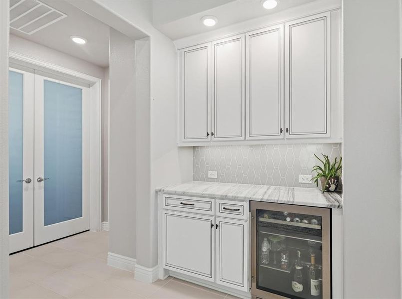 Built-in beverage station featuring white shaker cabinetry, marble-look countertops, and a full-height geometric tile backsplash