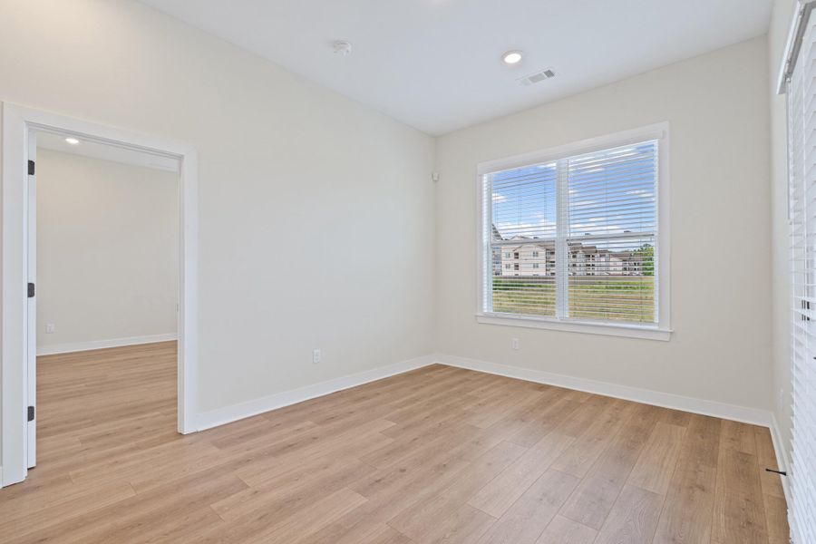 Room featuring wood-finish flooring, recessed lighting, and a large window with horizontal blinds Room featuring wood-finish flooring, recessed lighting, and a large window with horizontal blinds